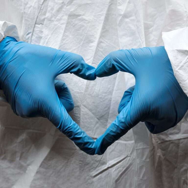 woman wearing ppe blue gloves making the shape of a heart with her fingers